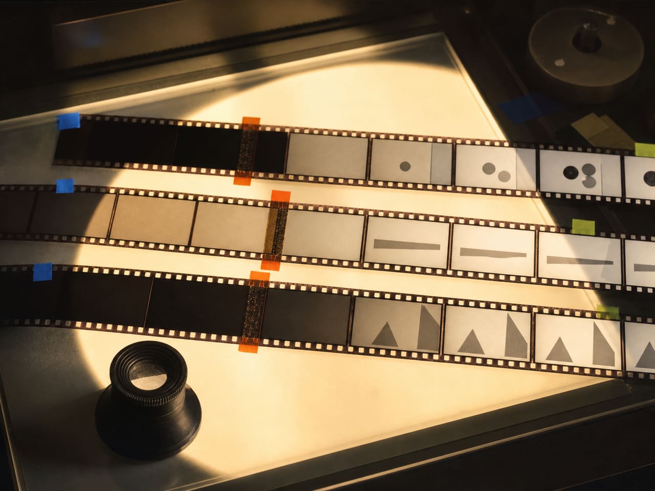 Benzi de film abstracte pe o masă luminoasă, cu cadre care devin vizibile la momente diferite